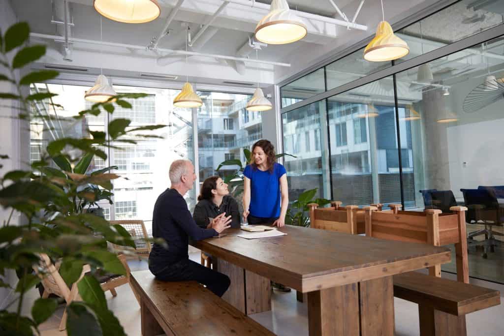 Three people standing over a long wooden table in Shopify’s office